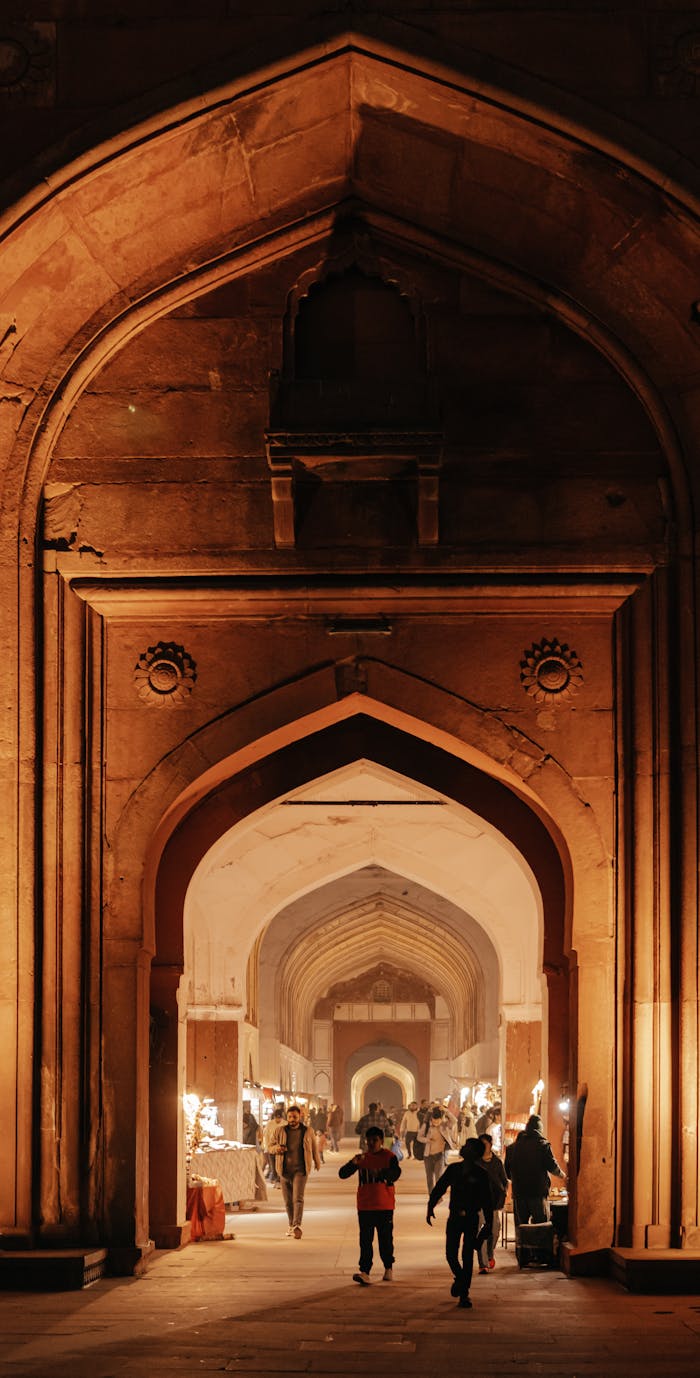 People walking through a beautifully illuminated archway at a historic Indian landmark.